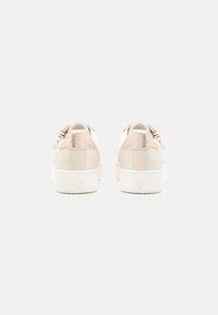 Sneaker bianco con retro beige testurizzato, tessuto liscio, dettagli in metallo dorato e suola bianca piatta.