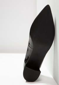 Chaussure noire à talon haut et bout pointu vue par le dessous, montrant la texture de la semelle et la taille 37.