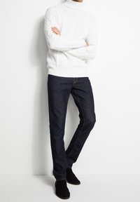 Pull en maille écrue à col roulé, jean slim bleu foncé et bottines en daim noires. Ensemble de mode simple et texturé.