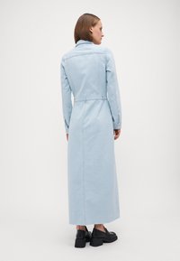 Svetlo modré denimové maxi šaty s dlhými rukávmi, pásom na zaväzovanie na chrbte a bočnými rozparkami, s golierom a gombíkovými manžetami.