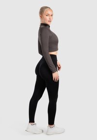 Zwarte high-waisted leggings en een aansluitende donkergrijze lange mouw crop top, beide gemaakt van rekbare stof met een subtiele ribbelstructuur.