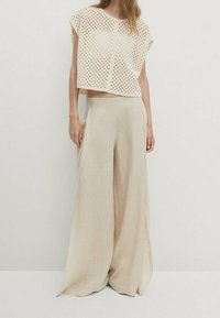 Beige, perforierter, gekürzter Oberteil mit kurzen Ärmeln, kombiniert mit weit geschnittenen, hellbeigen Hosen. Beide Teile haben ein lockeres, fließendes Design.