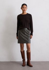 Pull noir duveteux, jupe en cuir olive et bottes marron jusqu'au genou. Design simple à col ras du cou ; texture lisse ; matériel minimal.