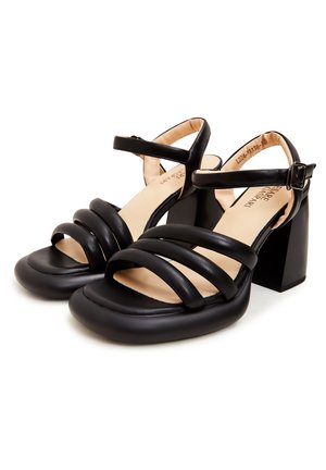 Schwarze Absatzsandalen mit mehreren gekreuzten Riemen, einer quadratischen Zehenpartie und einem klobigen Absatz mit glatter Textur und beigem Innenfutter.