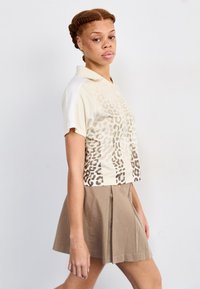 Kortärmad polo t-shirt i beige med ett leopardmönster, kombinerad med en veckad kaki kjol. T-shirten har en krage och kontrasterande ärmar.