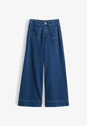 Jeans di denim blu a gamba larga con tasche applicate frontali, passanti per cintura e chiusura con bottone, mostrati su uno sfondo bianco.