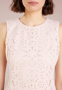 Robe rose clair avec un motif texturé semblable à de la dentelle et un col rond. Design sans manches avec des détails découpés complexes sur toute la surface.