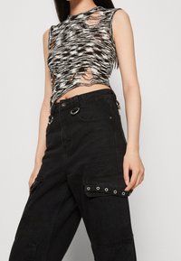 Top de punto recortado en blanco y negro con un patrón en ondas y múltiples agujeros desgastados, combinado con pantalones cargo negros de tiro alto con ojales.