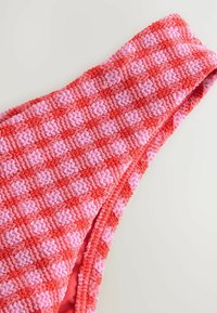 Stickad bikinitopp med ett mönster av växlande röda och rosa zigzag-designs, med en texturerad yta och tjocka band för stöd.