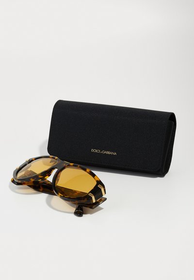 Ochelari de soare cu un model de țestoasă, cu lentile supradimensionate și accesorii din aur, însoțiți de o carcasă rigida neagră cu branding auriu.