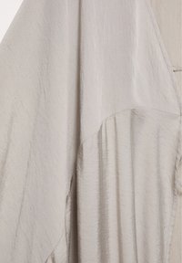 Gros plan d’un tissu beige avec une texture subtile et des détails de couture créant des plis doux.