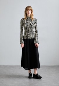 Maglione a righe bianche e nere con maniche lunghe, abbinato a una gonna nera a pieghe fluida. Il modello indossa scarpe nere chunky.