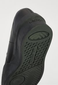 Μαύρη σόλα παπουτσιού Lacoste με υφές και σχέδια πρόσφυσης, καθώς και το λογότυπο Lacoste ανάγλυφο στην περιοχή της φτέρνας και στο κεντρικό ελαστικό μέρος.