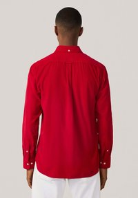 Camisa roja de manga larga con collar y puños abotonados, hecha de una tela suave, con detalle de canesú y un diseño de corte recto.
