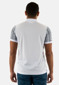 Maglietta atletica bianca a maniche corte, con accenti grigi a motivo e logo sulle spalle. Tessuto liscio, design sportivo.