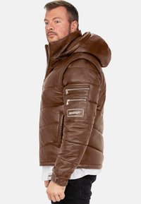 Giacca puffer in pelle marrone con cappuccio, caratterizzata da una trapuntatura orizzontale e tasche con zip sulle maniche. Finitura testurizzata e patch con logo.