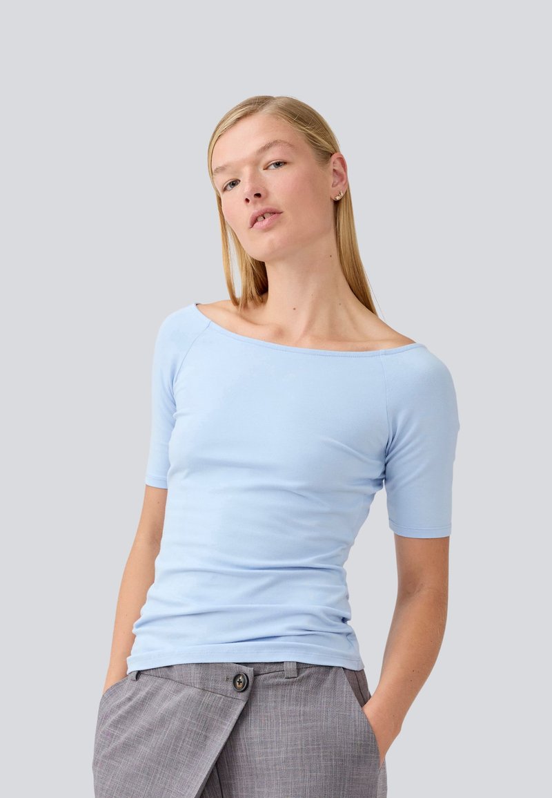 Lichtblauw, top met korte mouwen en een off-shoulder ontwerp, gemaakt van een gladde stof. Draagt het met lichtgrijze broeken met knoopaccenten.
