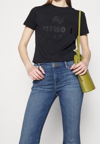 Musta puuvillainen t-paita, jossa on kohokuvioitu kirjailu "MISSONI MILANO". Siniset farkut ja pieni, pyöreä vihreä nahkalaukku.