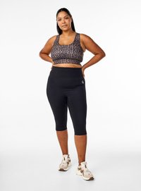 Schwarze Capri-Leggings kombiniert mit einem braunen Leopardenmuster-Crop-Top; die Leggings haben einen breiten Taillenbund und keine sichtbaren Verschlussdetails.