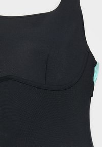 Maillot de bain noir avec une texture lisse, présentant un col rond et un accent teal d'un côté. Fines bretelles et doublure douce.