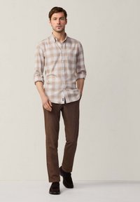 Camisa de cuadros beige con acentos marrones, mangas enrolladas; pantalones marrones, zapatos oscuros. Diseño simple con colores contrastantes.