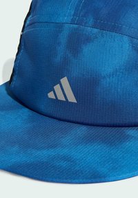 Gorra azul con un tejido texturizado y un patrón degradado, detalles en negro y un logo plateado de Adidas en la parte frontal.