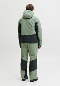 Waterproof jacket and pants in light green and black, featuring a hood, color-block design, and adjustable cuffs. Durable fabric with smooth texture.