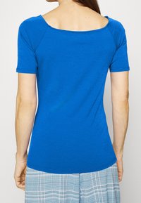 Top blu corto a maniche corte con scollatura a barca, realizzato in un tessuto morbido e leggero. Presenta una silhouette aderente e lievi costine lungo le cuciture.
