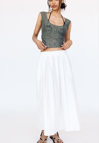Top corto in pizzo verde con maniche corte, abbinato a una lunga gonna di cotone bianco. L'outfit presenta una vestibilità comoda e sandali neri semplici.