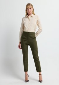 Beige overhemd met knopen gecombineerd met donkergroene, op maat gemaakte broek met hoge taille en slanke pasvorm, aangevuld met bordeauxrode hakken.