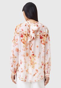 Bloes met bloemenpatroon in lichtroze stof, versierd met oranje en gele bloemen, lange mouwen en een sluiting met strik aan de achterkant, met een geraffineerde halslijn.