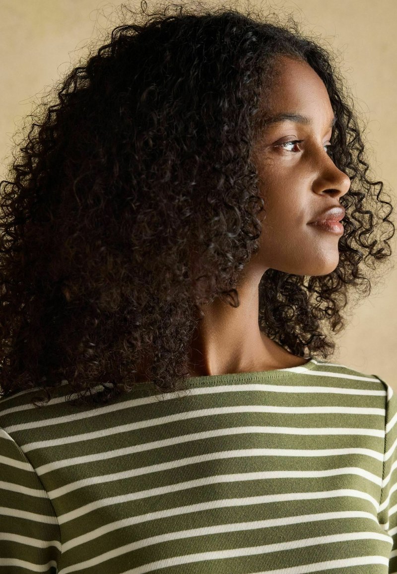 Roheline triibuline kudum, millel on laiad valged triibud, laevaninaline kaelus ja pehme tekstuur. Mudeli lokkis juuksed toovad disaini välja.