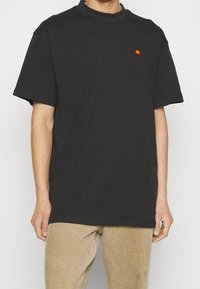 T-shirt en coton noir à coupe décontractée, avec un petit logo multicolore sur la poitrine. Manches courtes et col rond simple.