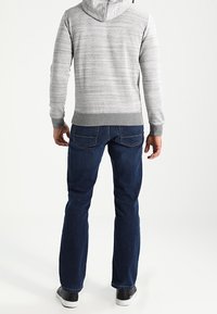 Sudadera con capucha a rayas grises, puños y dobladillo acanalados, combinada con jeans de mezclilla azul oscuro y zapatillas negras. Vista trasera visible.