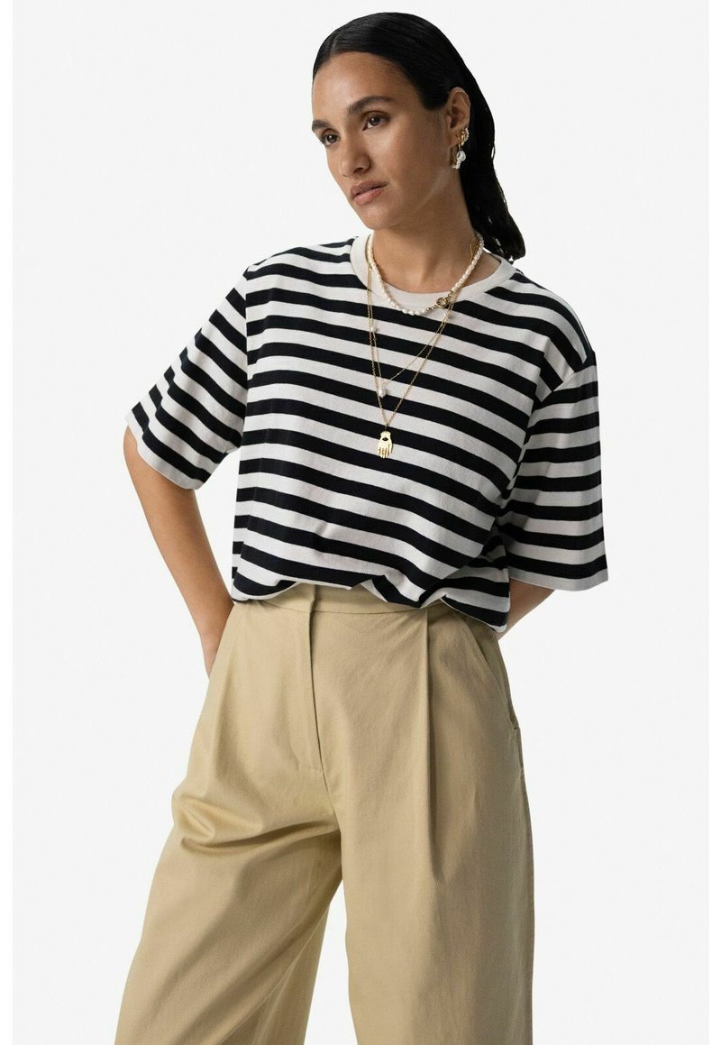 T-shirt à rayures noires et blanches à manches courtes avec un col rond, associé à un pantalon beige taille haute, offrant une coupe décontractée.