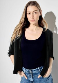 Svart lätt cardigan över en marinblå tanktop, matchad med ljusblå denimjeans. Släta texturer och avslappnad passform.