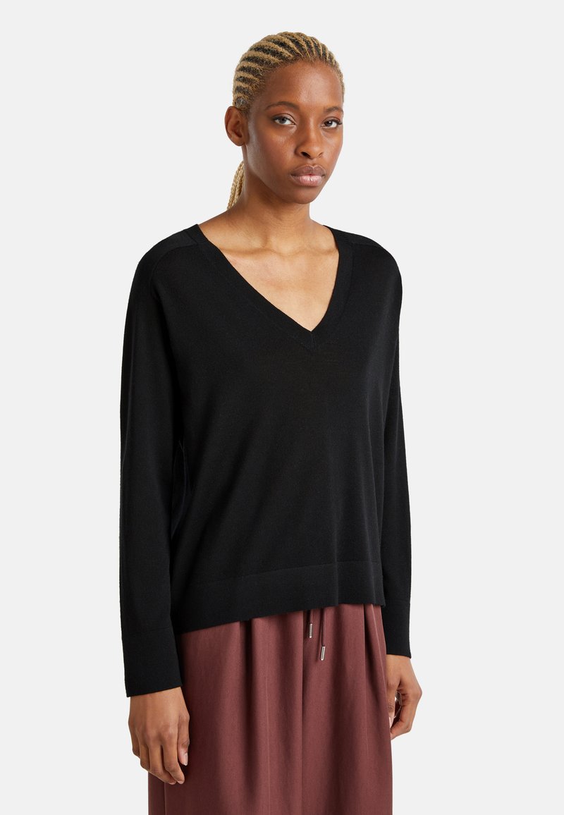 Maglione nero a scollo a v realizzato in un materiale morbido, con maniche lunghe e una vestibilità rilassata; presenta un orlo a coste e spacchi laterali, indossato su una gonna marrone.