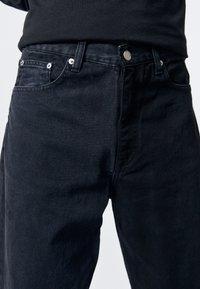 Tmavě modré denimové džíny s klasickým pětiokým designem, stříbrnými komponenty a jemnými detaily v šití. Materiál má hladkou strukturu.