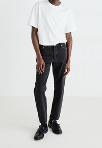 Camiseta blanca de algodón con cuello redondo combinada con jeans negros de pierna recta y mocasines negros, con un diseño minimalista y hardware sutil.
