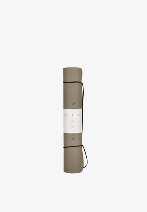 Esterilla de yoga beige enrollada, asegurada con correas negras y una banda con etiqueta blanca que muestra la marca y texto del producto.