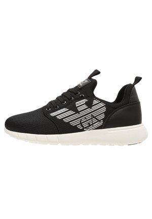 Czarny niski sneaker z białą podeszwą, wiązany na sznurówki, z pętlami do ściągania i dużym białym stylizowanym logo na bocznej części.