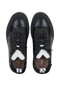 Schwarze Ledersneaker mit strukturierter Oberfläche, kontrastierenden weißen Akzenten, schwarzen Schnürsenkeln und genoppter Gummisohle. Sichtbares Gold-Branding-Detail.