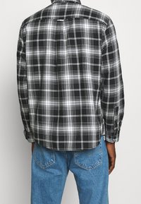 Camicia a quadri bianco e nero con maniche lunghe, colletto a bottoni e piega sul retro. Indossata con jeans in denim blu, vista da dietro.
