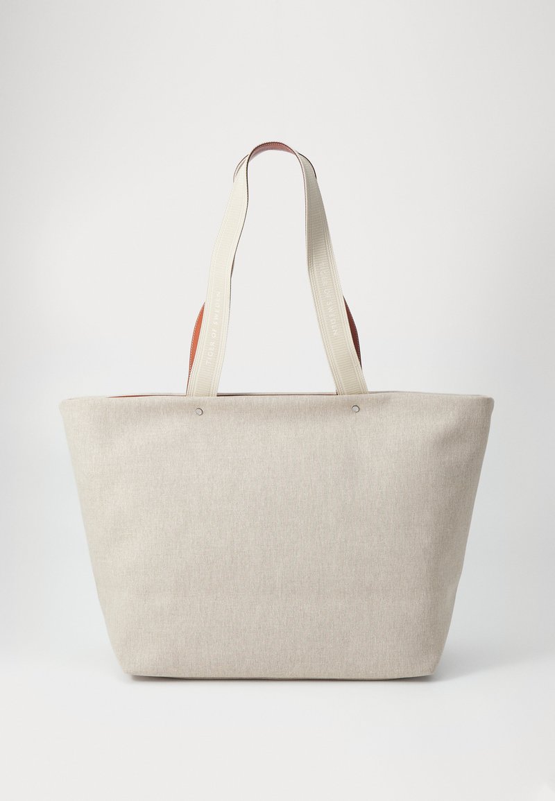 Tote bag mare de culoare bej, realizat dintr-un material texturat, având două mânere lungi și rezistente de culoare crem și accente maro în partea de sus.