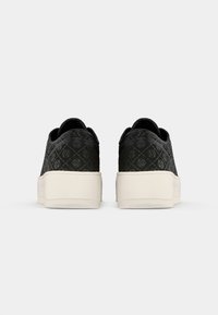 Un paio di sneakers platform nere con tomaie decorate e suole bianche spesse, mostrate da dietro su uno sfondo chiaro e semplice.