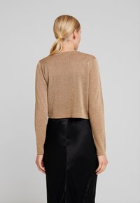 Croppad långärmad topp i glansigt guldtyg med en slät textur. Kombinerad med en svart satinkjol som skapar kontrast i färg och glans.