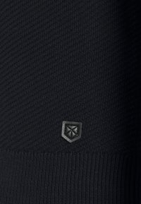 Svart stickad tröja med ribbad nederkant, med ett strukturerat mönster och en liten mörk emblem i den nedre delen.