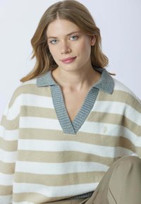 Maglione a righe con scollatura a V. Presenta strisce alternate beige e bianche e un colletto a coste grigio chiaro. Tessuto morbido e testurizzato.