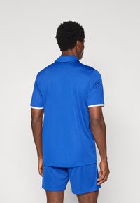 Βασιλικό μπλε πόλο πουκάμισο με γιακά και λευκή λεπτομέρεια, συνδυασμένο με αντίστοιχα σορτς. Ελαφρύ ύφασμα, ομαλή υφή. Εμφανίζεται η πίσω όψη.