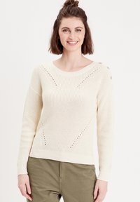 Cream-colored knitted sweater with a ribbed texture, featuring diagonal pattern accents and decorative buttons on the shoulder.